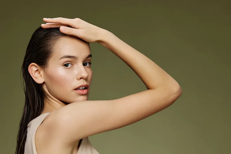 Young woman with wet hair poses against a green background, showcasing natural beauty and confidence in a neutral outfit, ideal for health and beauty concepts