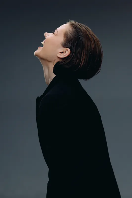 Laughing woman in black outfit looking up with joy and confidence on dark background