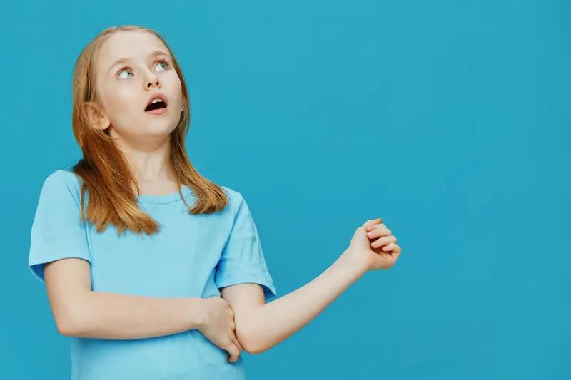 A young girl with long brown hair looking upward, dressed in a light blue t shirt, displaying a surprised expression, with a solid blue background