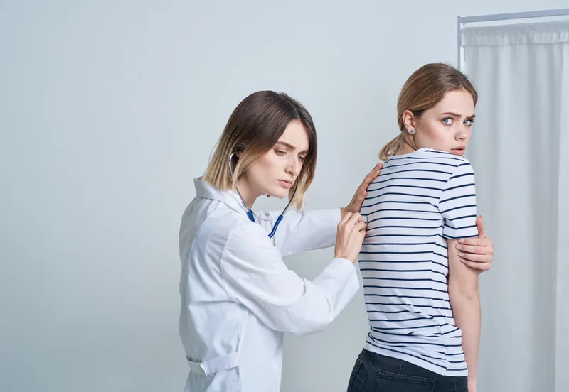 Женщина-врач в медицинском халате со стетоскопом слушает сердце пациента