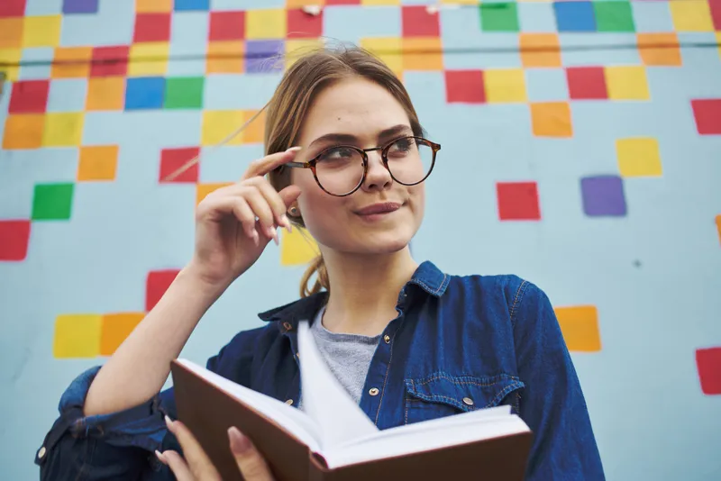 Удивленная студентка в очках на улице с книгой, эмоции, модель