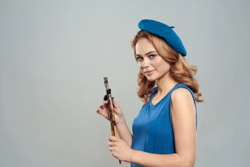 Женщина-художница с кистью в руке, в синем берете и платье