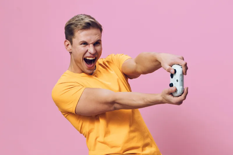 Young cheerful man in bright yellow t-shirt taking a selfie with smartphone, expressing happiness and excitement, pink background, portrait-style, lifestyle concept.