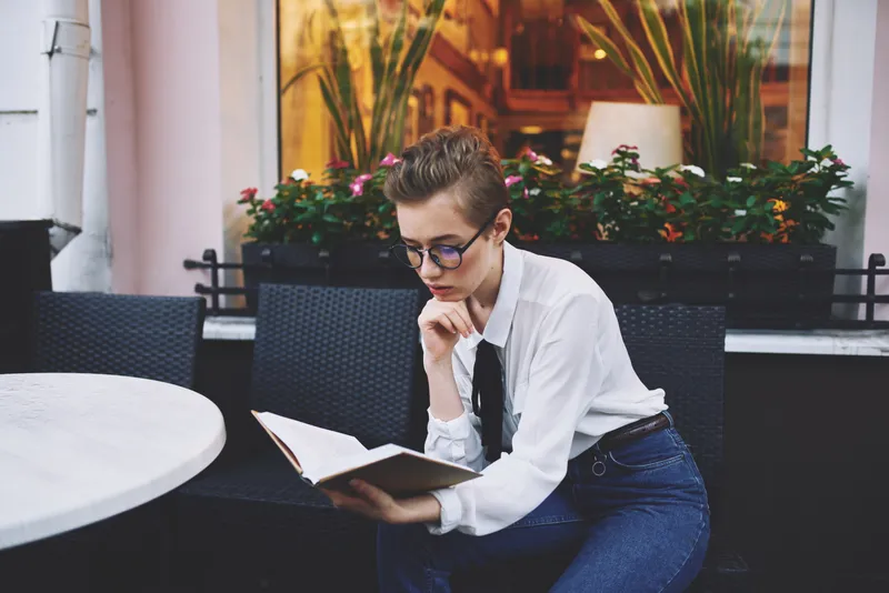 Коротко стриженная женщина держит в руках книгу и читает, занимаясь самообразованием