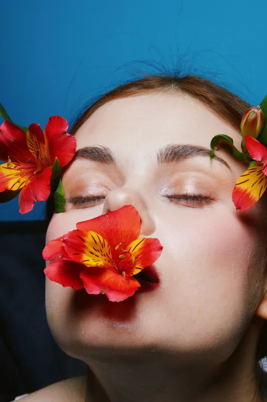 A serene woman with flowers on her face, embodying beauty and calmness against a vibrant blue background, showcasing emotions of tranquility and nature