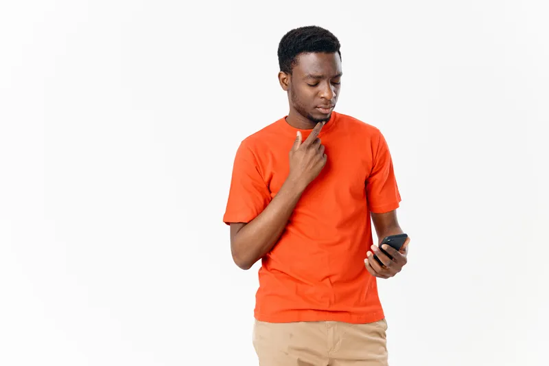 Афроамериканский парень в оранжевой футболке с мобильным телефоном на светлом фоне