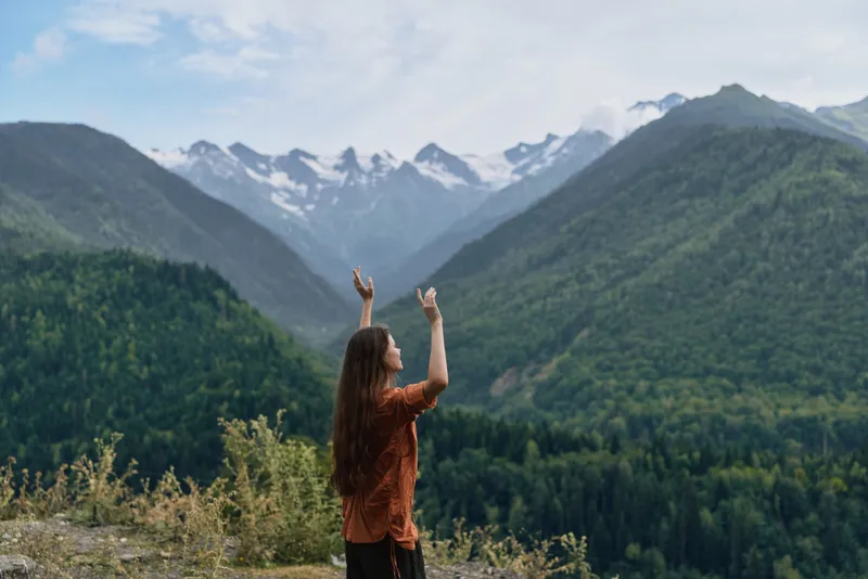 Mountains nature landscape wilderness hiking woman outdoors with arms raised admiring valley and distant snowcapped peaks in a vast scenic setting during daytime