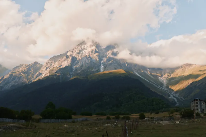 A tranquil mountain landscape unfolds with dramatic clouds over rugged peaks and a sunlit valley, inviting quiet exploration and a sense of freedom.