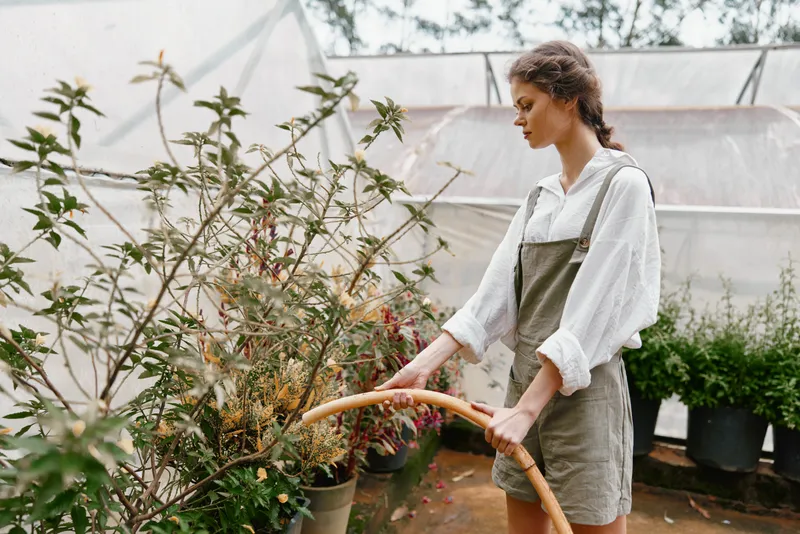 Young woman tending to plants in greenhouse, wearing casual overalls, natural emotion, cozy atmosphere, showcasing sustainable gardening practices