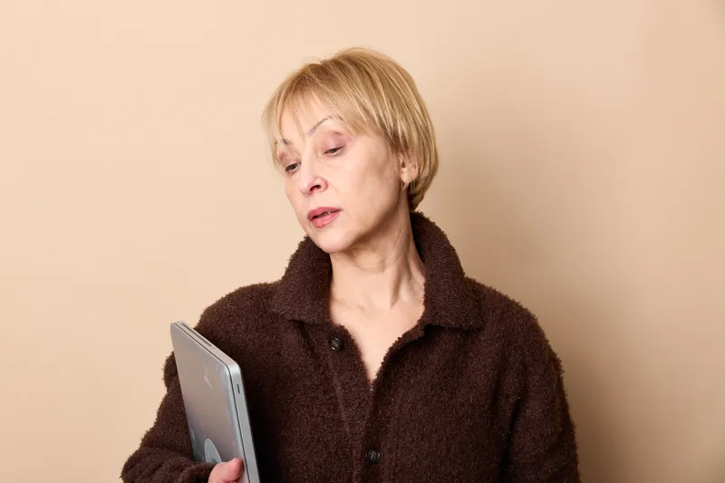 Woman, senior, tablet, technology, communication, concern, reading, indoors, portrait, studio, female reads on tablet, anxious expression, beige background