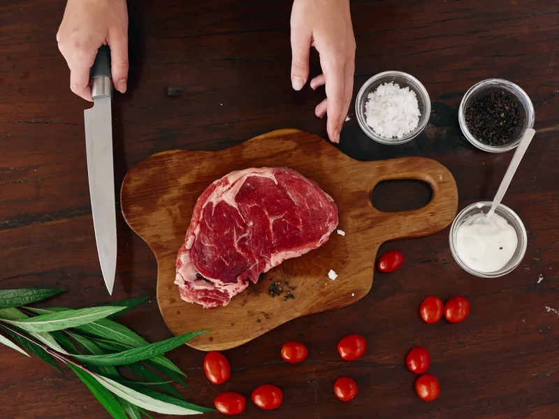 Женщина с ножом в руке нарезает свежее мясо стейка для жарки на кухне