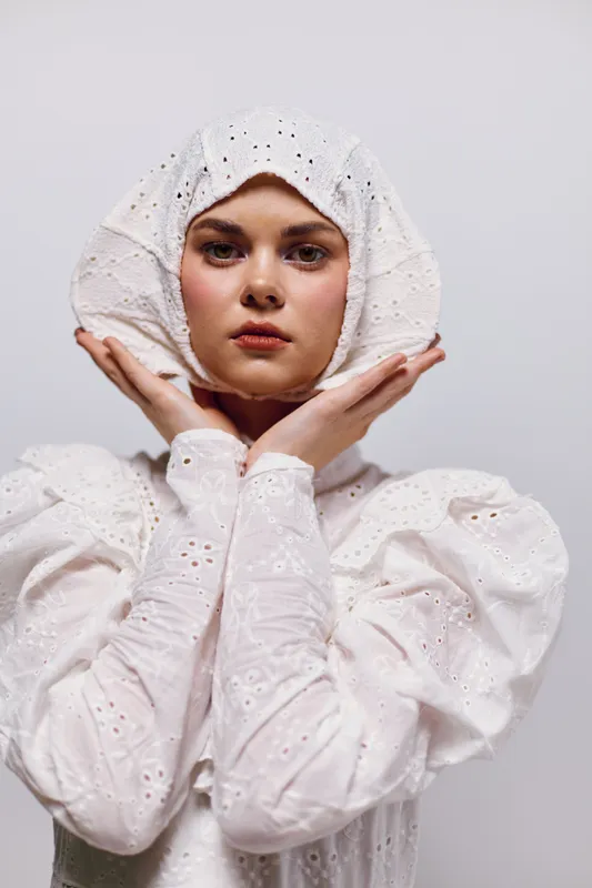 Ethereal young woman in a vintage white dress and headpiece, conveying serenity and elegance against a minimalist background Perfect for fashion and beauty concepts
