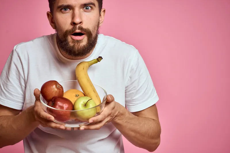 Энергичный мужчина со свежими фруктами в чашке на розовом фоне, свободное место