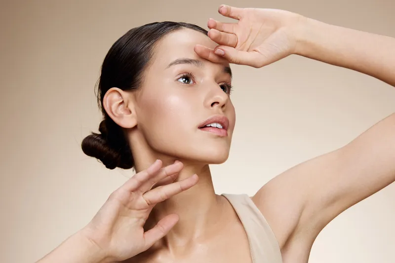 A young model with a serene expression poses elegantly against a soft, neutral background, showcasing natural beauty and skincare concepts in a warm, inviting setting