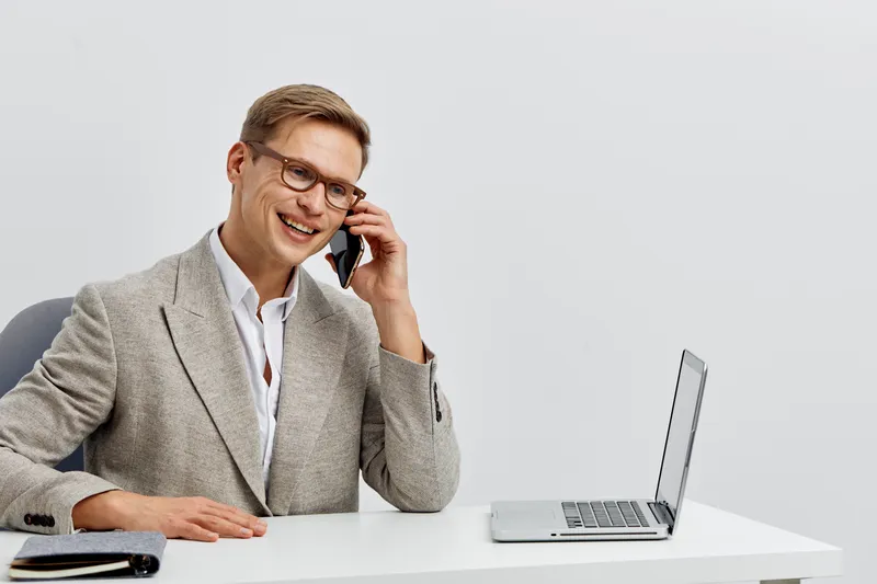 smiling man talking on phone work laptop business casual outfit digital nomad remote communication concept