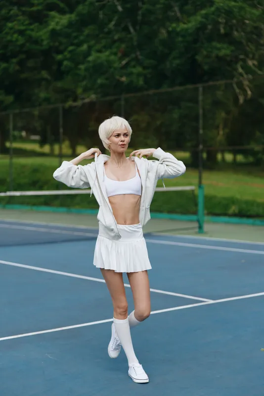 Stylish young female athlete in white activewear on a tennis court, portraying determination and focus while preparing for a match