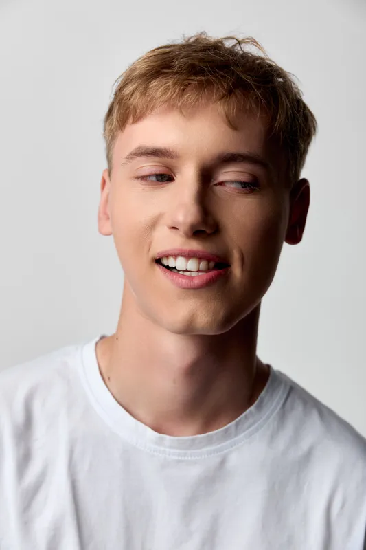 Young man in a white t shirt with a relaxed smile, casual headshot style, clean backdrop, natural expression, everyday fashion, approachable mood, soft lighting and neutral vibe