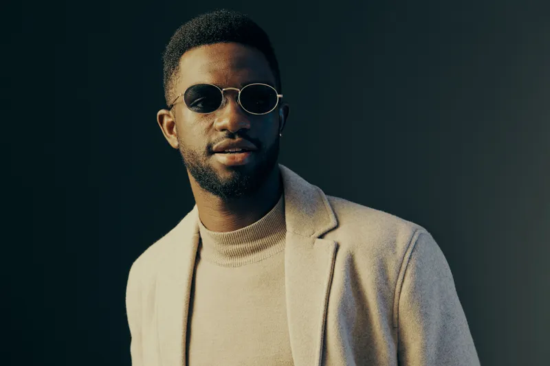 Stylish African man in sunglasses wearing a beige blazer, exuding confidence against a dark background, perfect for fashion and lifestyle content