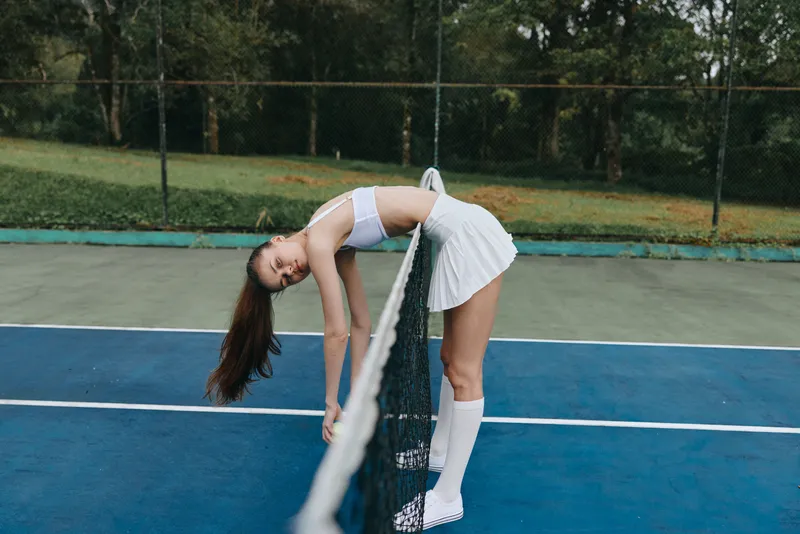 Young athletic female tennis player in white sports attire expressing joy on the court surrounded by greenery Fresh, vibrant colors expressing an active lifestyle