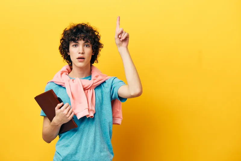 Парень учится с блокнотом, жестикулируя рукой, кадр обрезан