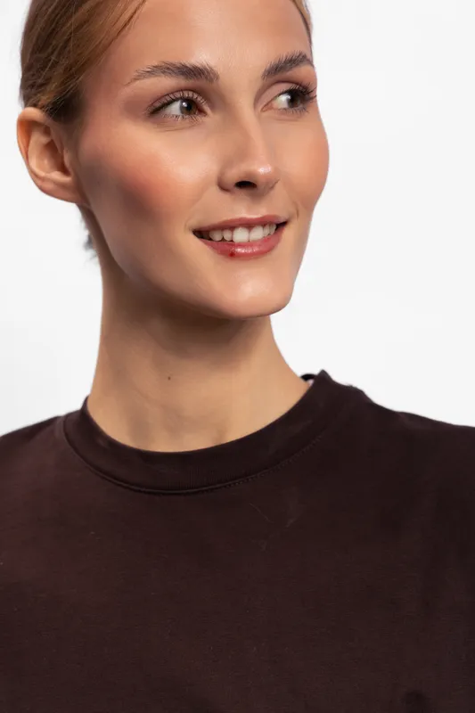 Young woman with clear skin and natural makeup smiles softly looking to the side. Casual style with brown shirt on white background. Concept for beauty and lifestyle.