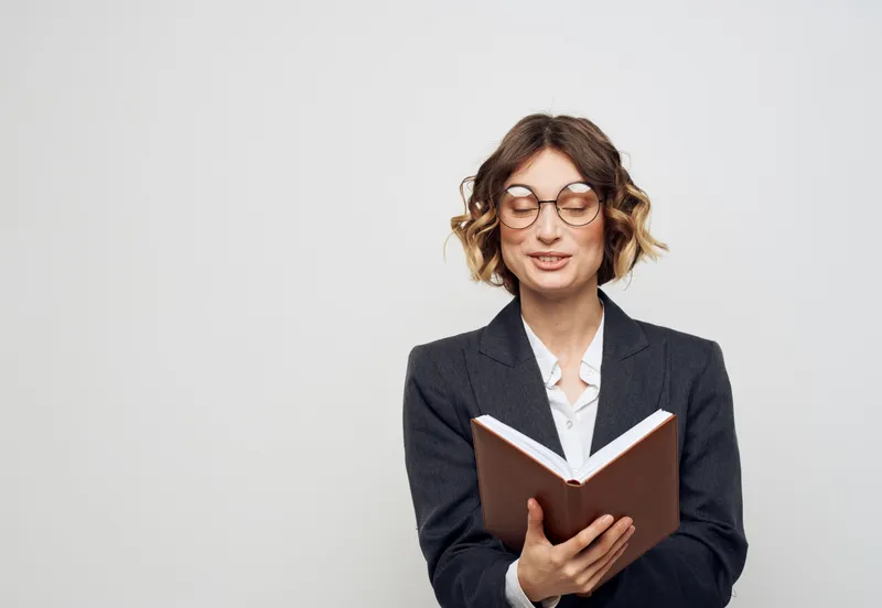 Женщина в классическом костюме с открытой книгой, в очках на лице, крупный план