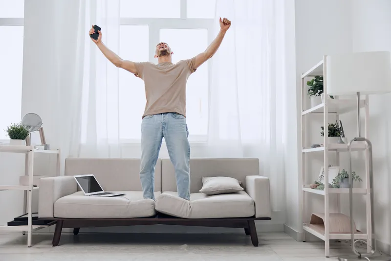 Excited man celebrating digital detox at home, showcasing joy amidst technology fatigue and promoting well-being and balance in life.