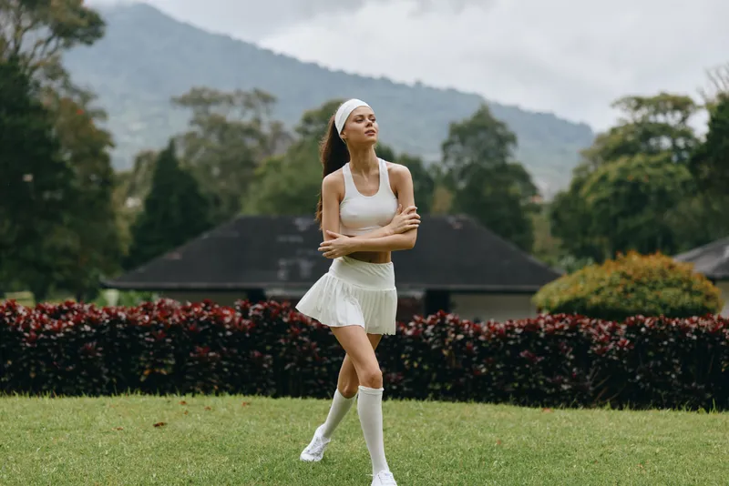 Elegant female model in white athletic wear enjoying a serene outdoor setting, exuding confidence and grace, surrounded by lush greenery
