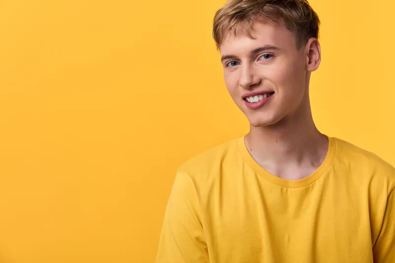 Man wearing a bright yellow shirt with a cheerful smile against a vivid yellow studio background, showcasing casual fashion and warm lighting for lifestyle and positivity