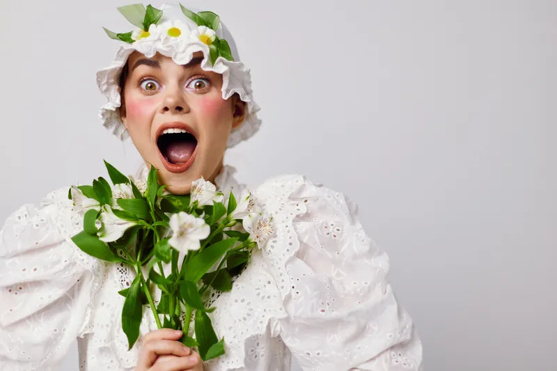 Cheerful young woman in a vintage white dress holding fresh flowers and expressing excitement with a joyful scream, conveying a sense of happiness and celebration
