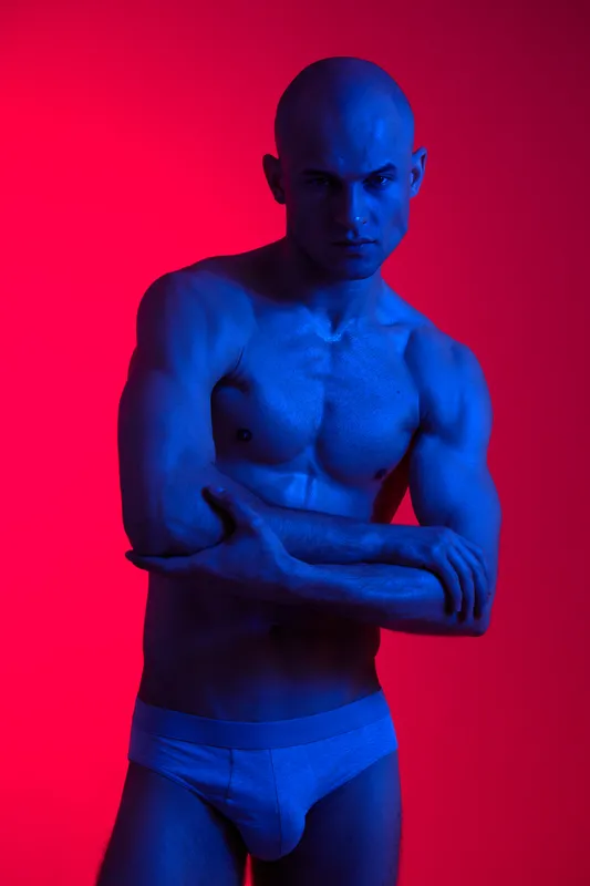 Athletic man posing confidently in blue lighting, showcasing strength and determination. This captivating portrait emphasizes body expression and mood.