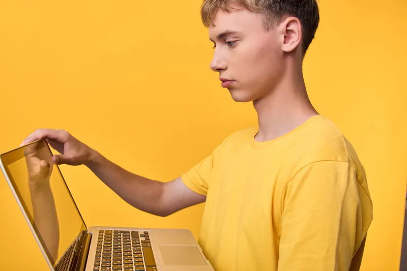 Young worker using a laptop against a bright yellow backdrop, focused on the screen, illustrating modern technology and creative digital workspace for online learning