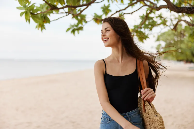 Женщина идет по пляжу с длинными волосами, развевающимися на ветру