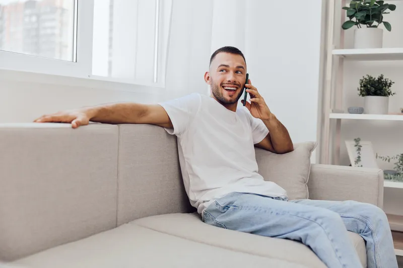 A joyful man on a phone call, embodying emotional connection and soft masculinity, reflecting a moment of authenticity and relaxation in a cozy home environment.