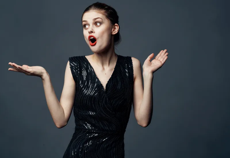 Женщина в черном платье жестикулирует руками, выражая удивление и восторг