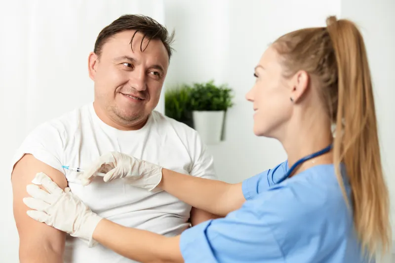 Пациент мужского пола находится в больнице рядом с врачом, который делает инъекцию