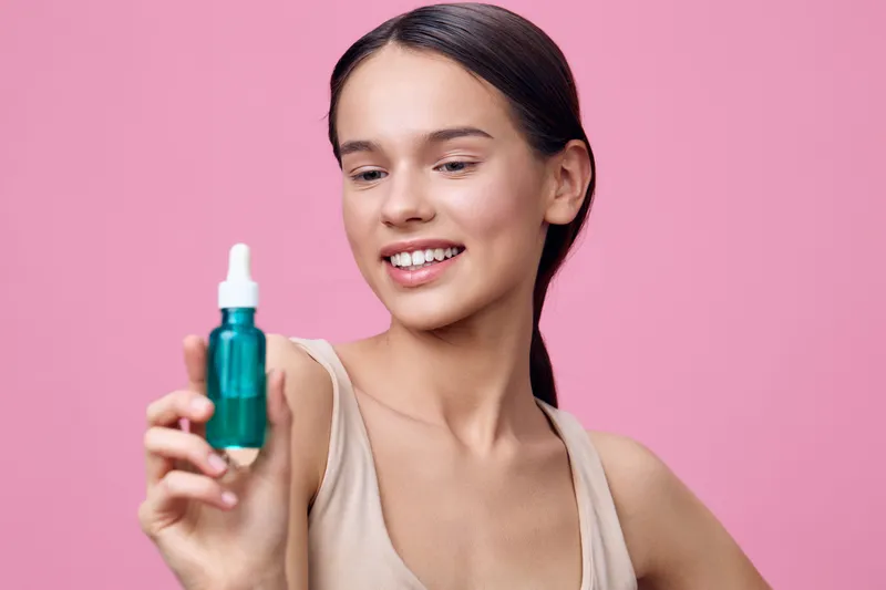 Young woman showcasing a green serum bottle, expressing joy against a soft pink background, highlighting beauty and skincare Perfect for healthy lifestyle concepts