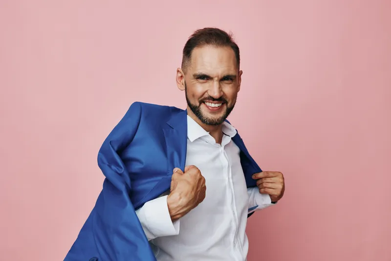 A professional man in a blue suit stands against an isolated pink colored background, exuding confidence, focus, and readiness for success in a corporate setting.