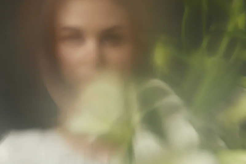 Soft focus portrait of a woman with natural makeup surrounded by greenery, conveying tranquility and a connection to nature, ideal for concepts of wellness and beauty