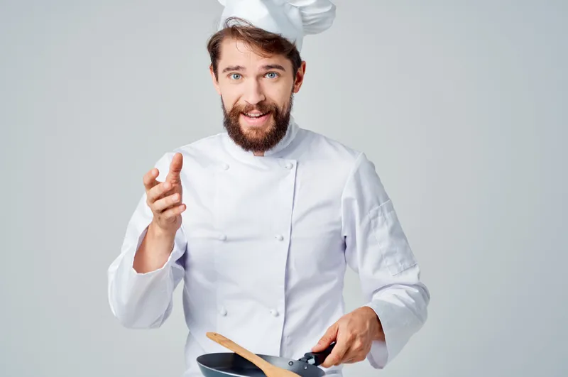 Повара со сковородой готовят еду в ресторанной кухне, на их лицах читаются эмоции