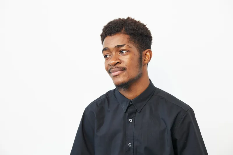 Black man wearing a black shirt, providing a thoughtful expression while looking off-camera, conveying a mood of contemplation and introspection.