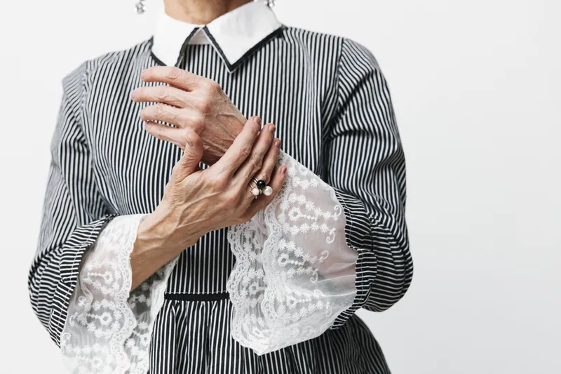 Стильная женщина в чёрно-белом полосатом платье позирует, скрестив руки на груди и глядя в камеру, изолированно на белом фоне