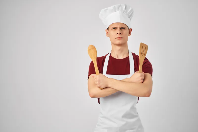 Повар-мужчина в белом фартуке с кухонной утварью готовит изысканную еду