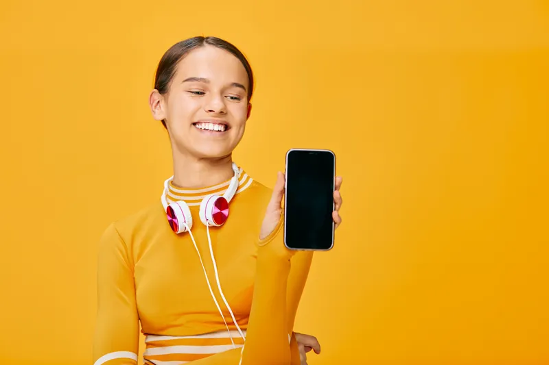 Fitness sport woman in a bright orange outfit holds a smartphone and headphones against a vibrant yellow background, illustrating an active lifestyle, music during workouts, and modern tech on the go.