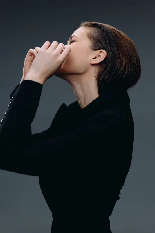 Pensive woman in black clothing with closed eyes expressing deep thought and calmness in a dark studio setting.