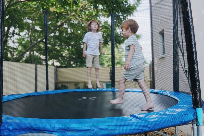 Playful children jumping on a trampoline, showcasing joy and energy in an outdoor setting filled with sunlight and greenery, perfect for family fun.
