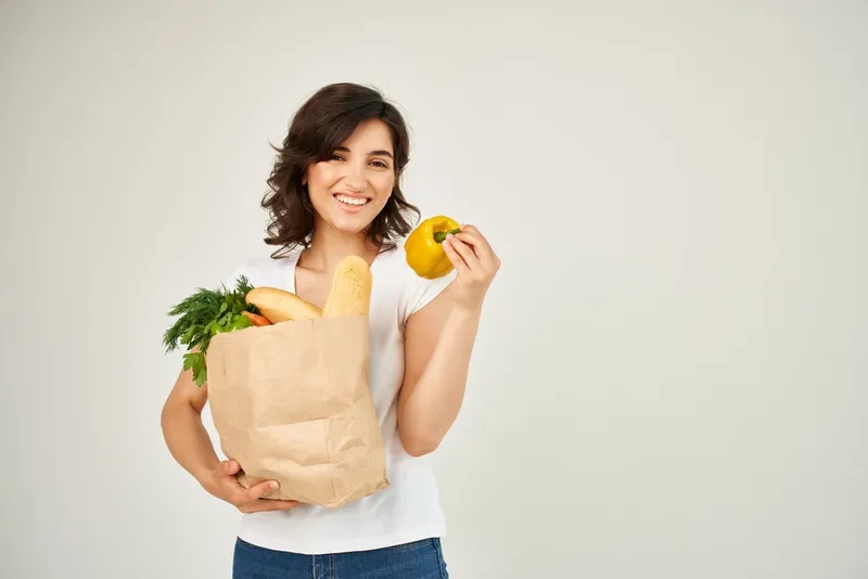 Весёлая женщина с пакетом продуктов здорового питания в супермаркете