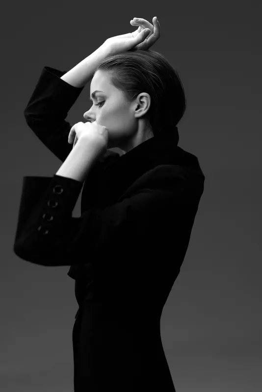 Black and white portrait of a thoughtful woman in a dark jacket posing with closed eyes in studio lighting.