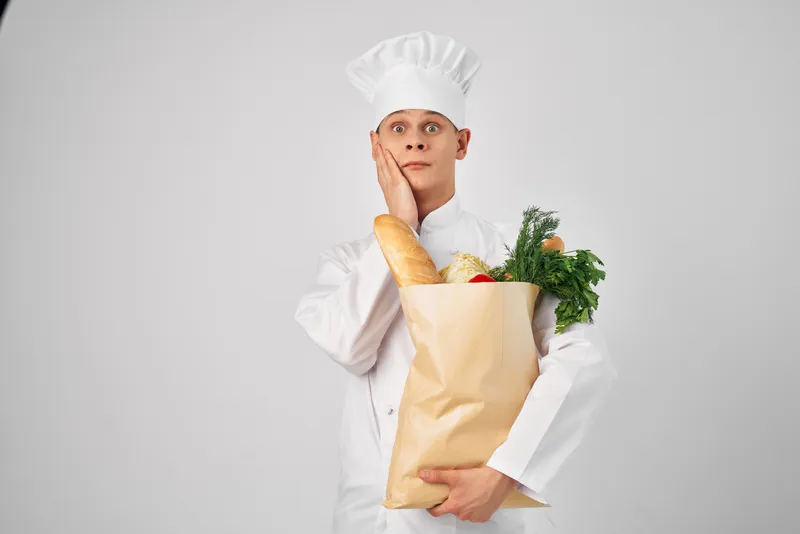 Весёлый шеф-повар мужского пола с упаковкой продуктов работает на кухне