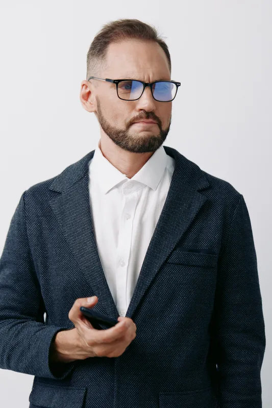 A professional male businessman stands against an isolated colored backdrop, projecting focus and confidence as he surveys a handheld device, ready to engage in strategic tasks.